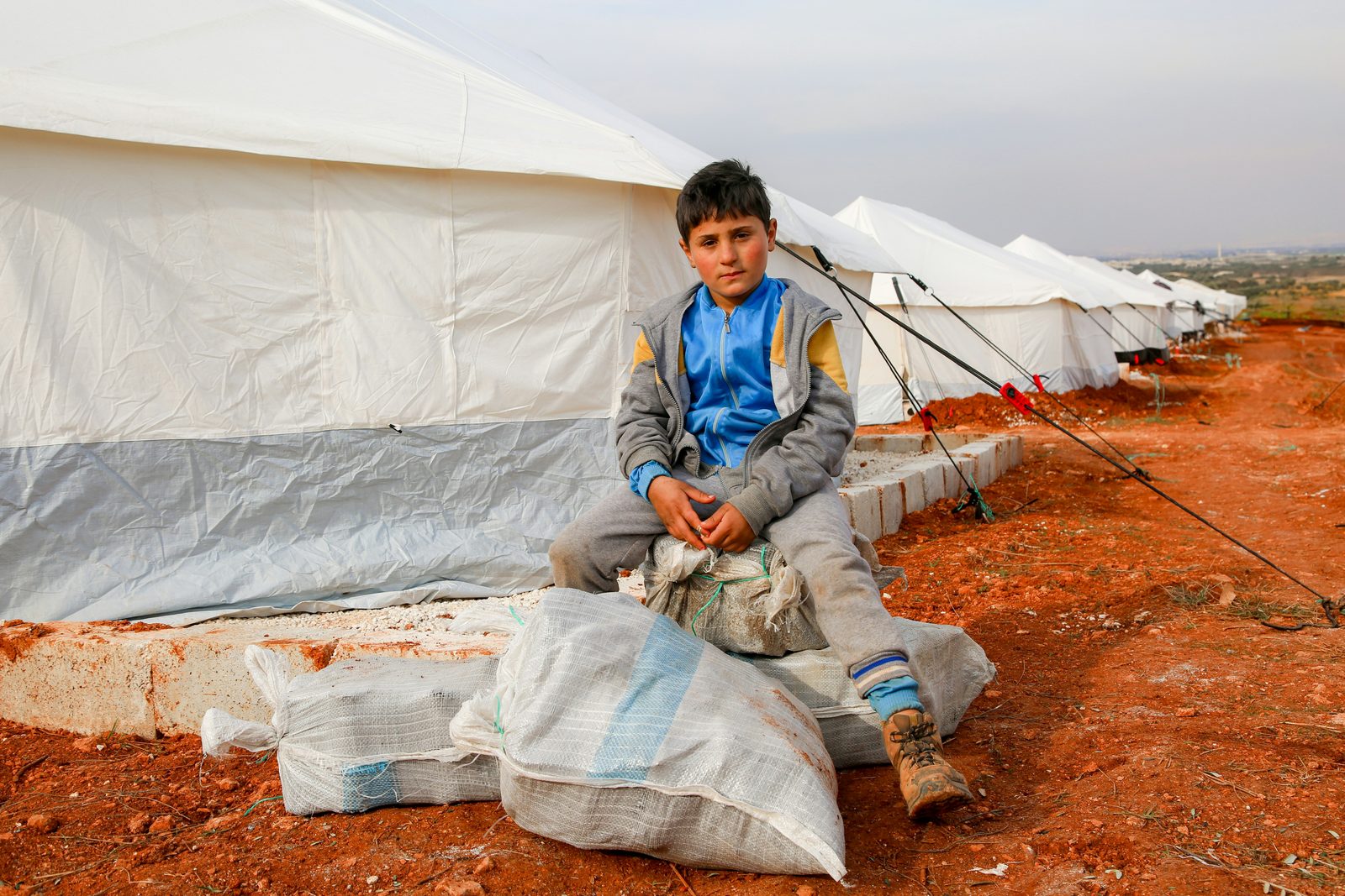 A boy sitting outside tents at a relief camp